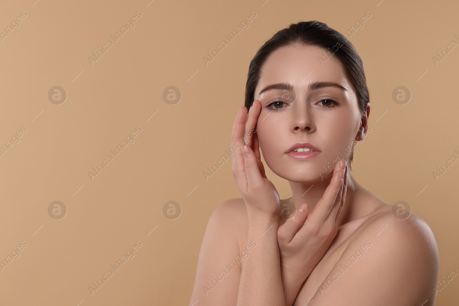 Photo of Young woman massaging her face on beige background. Space for text