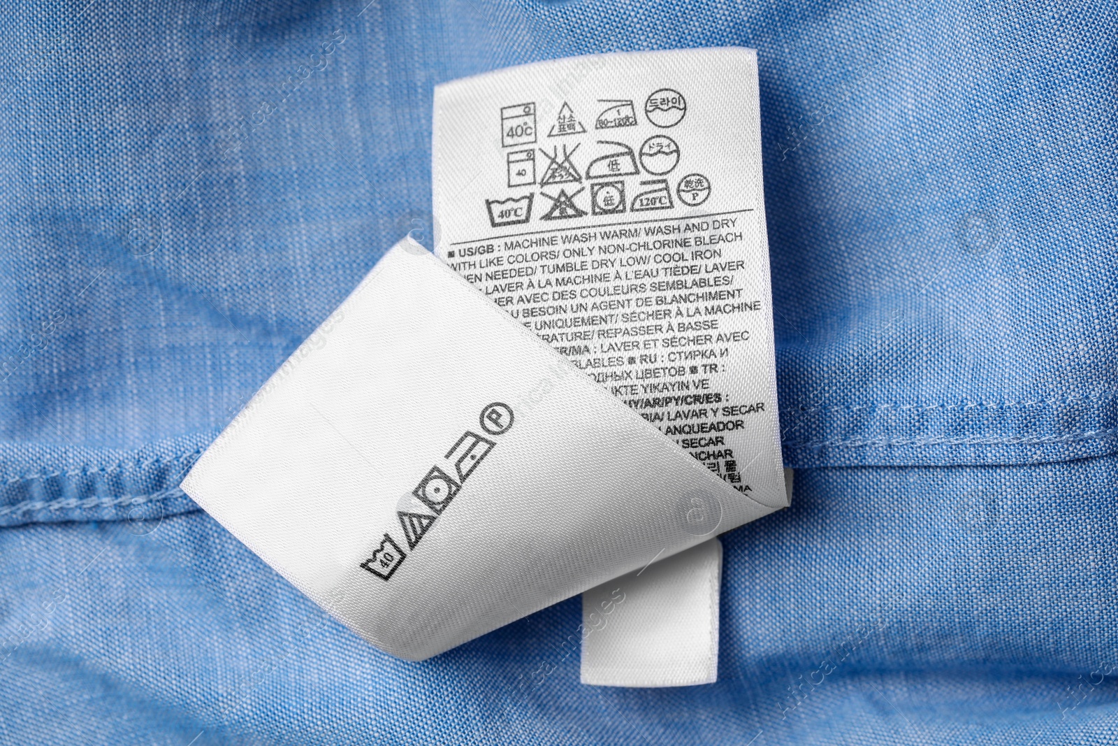 Photo of White clothing labels on light blue garment, top view