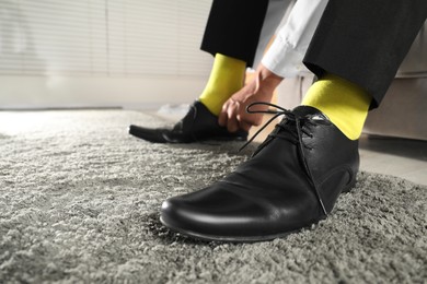 Photo of Man with yellow socks putting on stylish shoes indoors, closeup