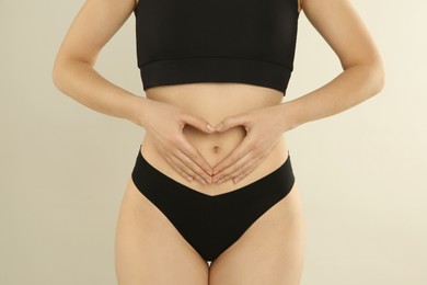 Photo of Gynecology. Woman in underwear making heart with her hands on light background, closeup