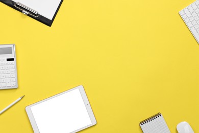 Modern tablet, keyboard and stationery on yellow background, flat lay. Space for text