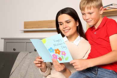 Happy woman receiving greeting card from her son at home