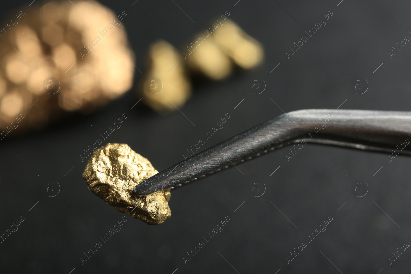 Photo of Tweezer with shiny gold nugget on blurred background, closeup