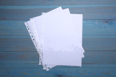 Punched pockets with paper sheets on light blue wooden table, flat lay