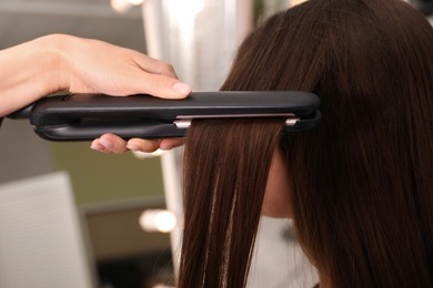 Photo of Stylist straightening woman's hair with flat iron in salon