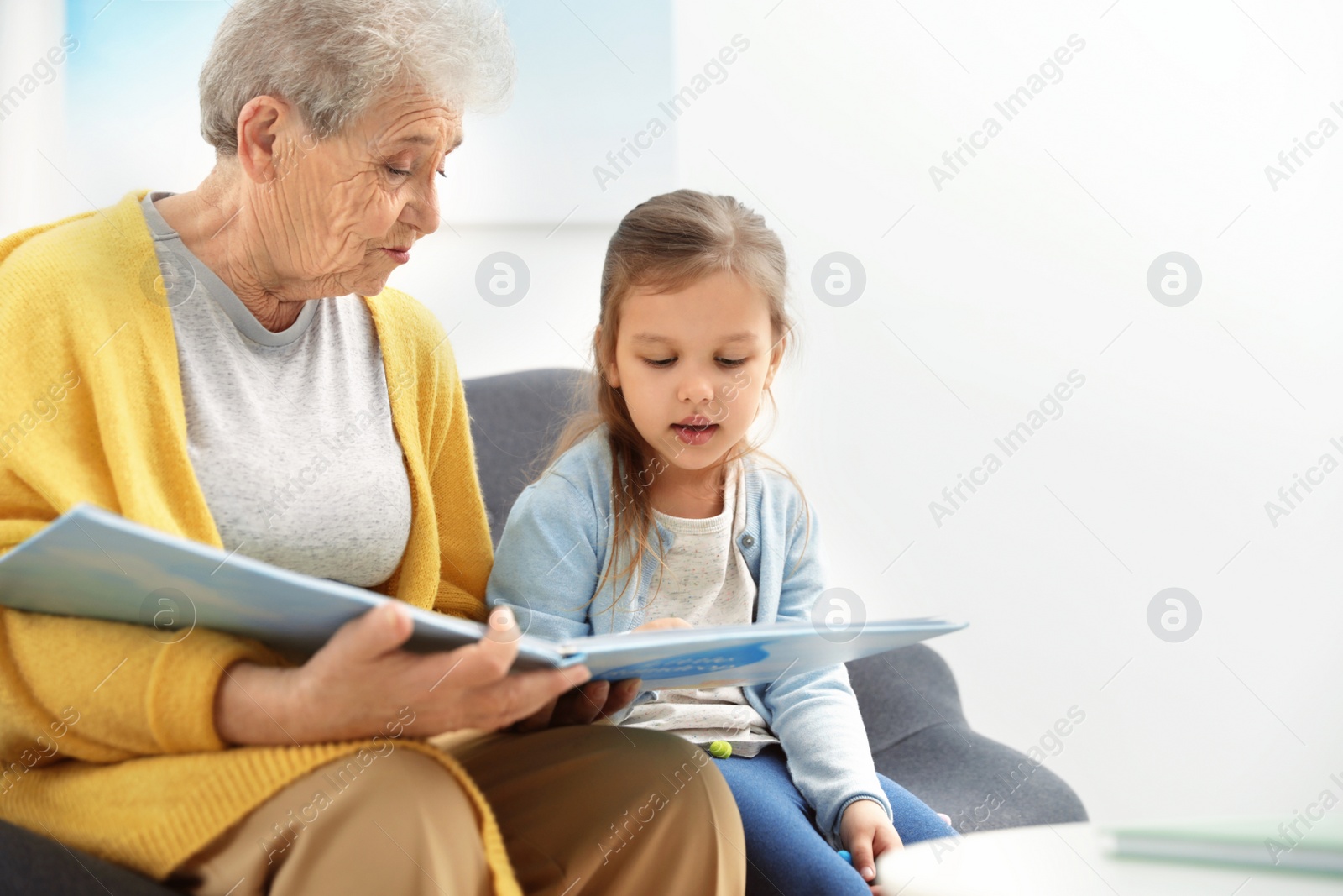 Photo of Cute girl and her grandmother reading book at home