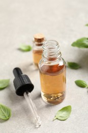 Photo of Bottles of essential basil oil and fresh leaves on light grey table