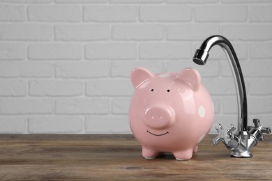 Photo of Water scarcity concept. Piggy bank and tap on wooden table, space for text