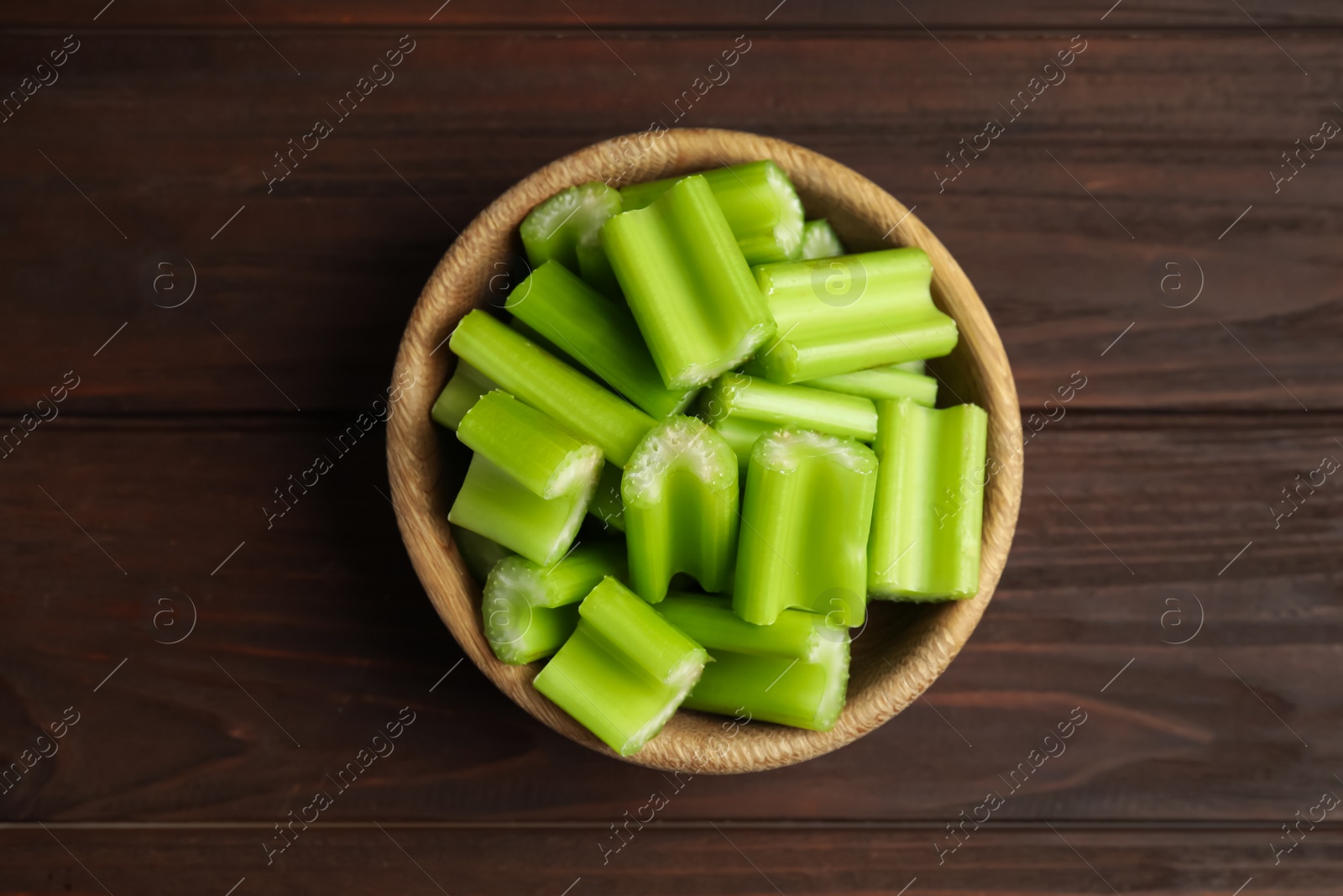 Photo of Cut celery in bowl on wooden table, top view