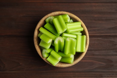 Cut celery in bowl on wooden table, top view