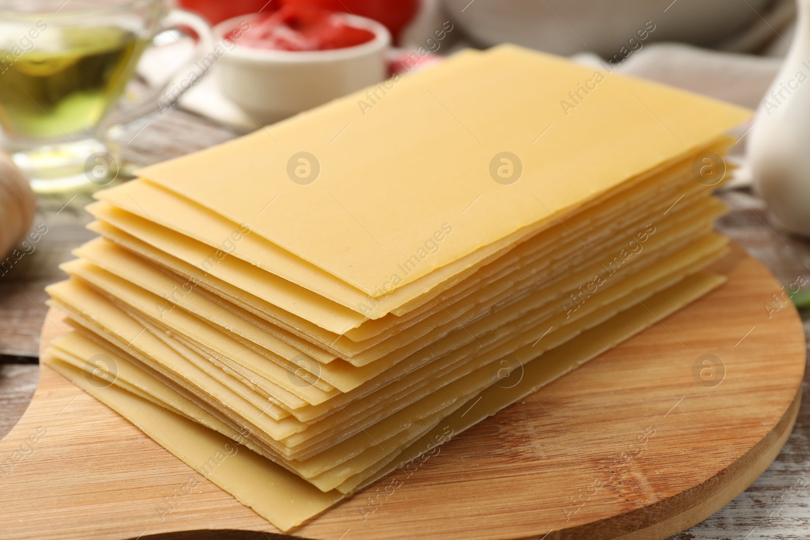 Photo of Cooking lasagna. Board with stack of pasta sheets on wooden rustic table, closeup
