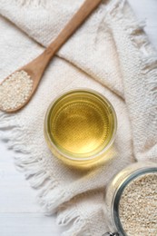 Photo of Jar of organic sesame oil and seeds on white wooden table, flat lay