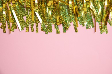Photo of Golden tinsel on pink background, top view. Space for text