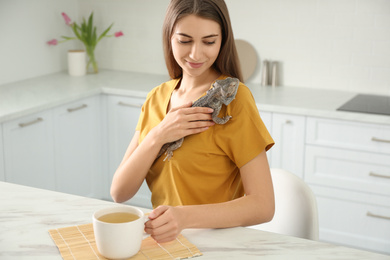 Photo of Woman holding bearded lizard in kitchen. Exotic pet