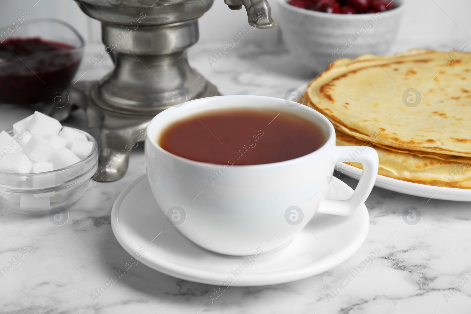 Photo of Metal samovar with cup of tea and treats on white marble table, closeup