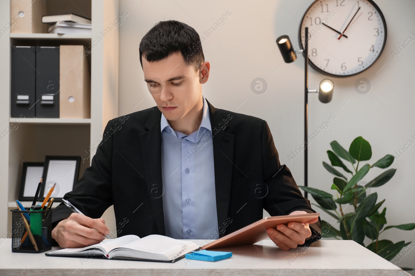 Photo of Man taking notes while using tablet at table in office