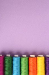 Photo of Different colorful sewing threads on lilac background, flat lay. Space for text