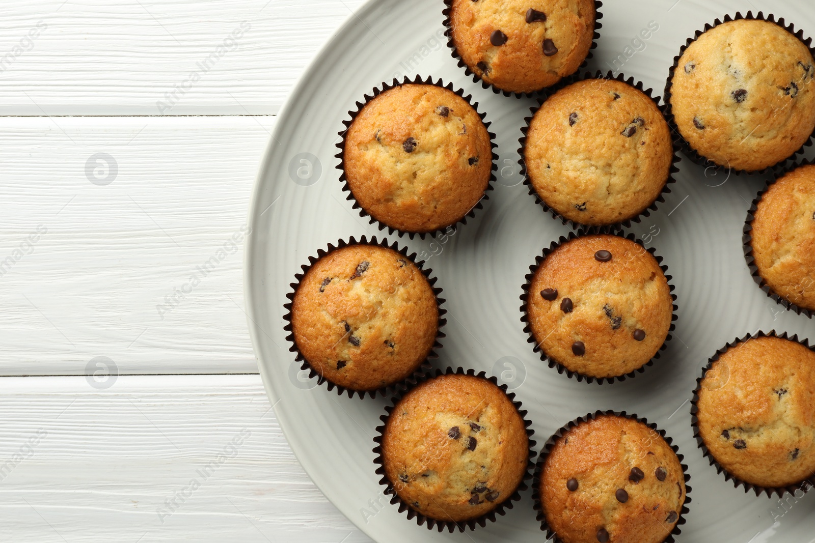 Photo of Delicious freshly baked muffins with chocolate chips on white wooden table, top view