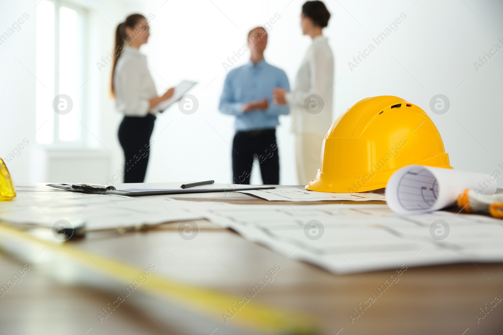 Photo of Colleagues in office, focus on table with construction drawings and tools