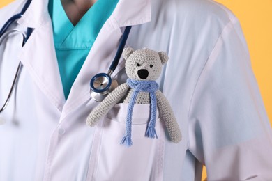 Pediatrician with toy bear and stethoscope on yellow background, closeup