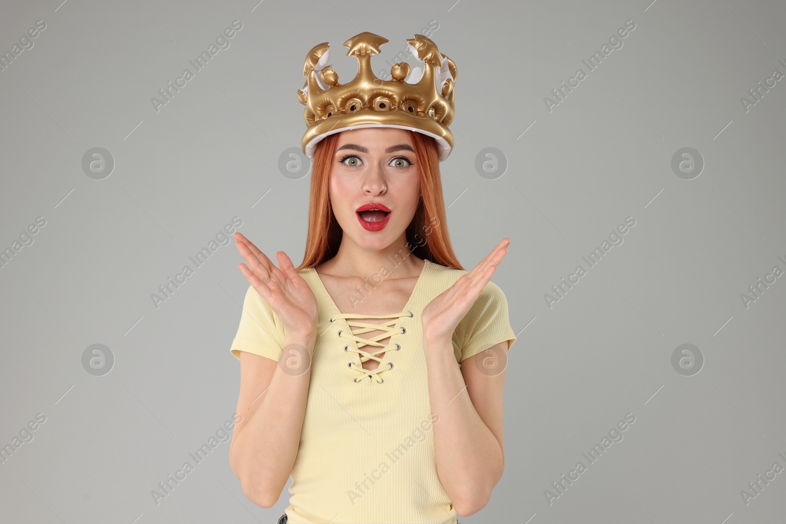 Photo of Emotional young woman with inflatable crown on light grey background