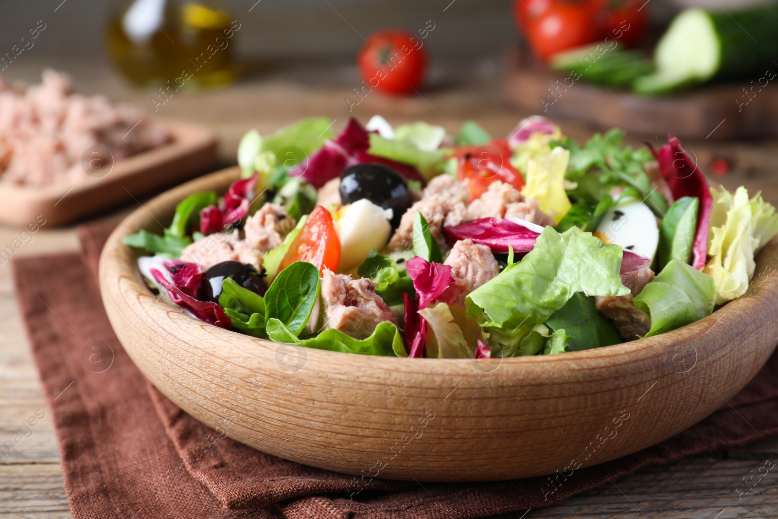 Photo of Bowl of delicious salad with canned tuna and vegetables on wooden table, closeup