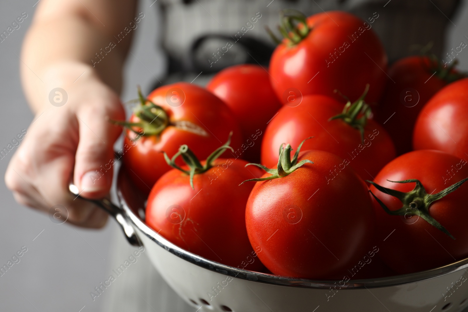 Photo of Woman with colander of ripe tomatoes on grey background, closeup