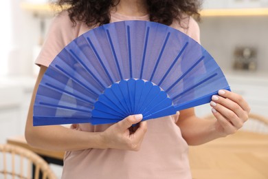 Photo of Woman with blue hand fan indoors, closeup