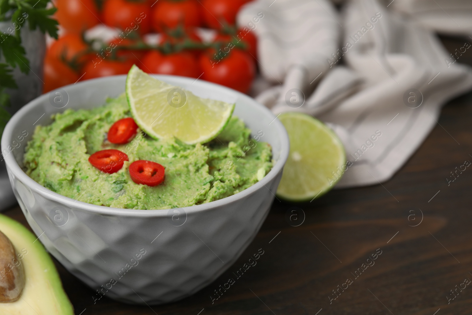 Photo of Bowl of delicious guacamole and ingredients on wooden table, closeup. Space for text
