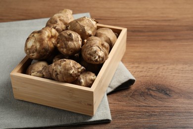 Photo of Crate with fresh Jerusalem artichokes on wooden table. Space for text