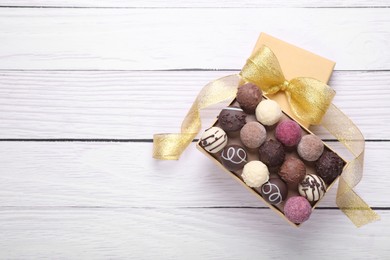 Photo of Open box with delicious chocolate candies on white wooden table, top view. Space for text