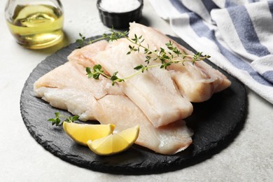 Photo of Pieces of raw cod fish and lemon on light grey table