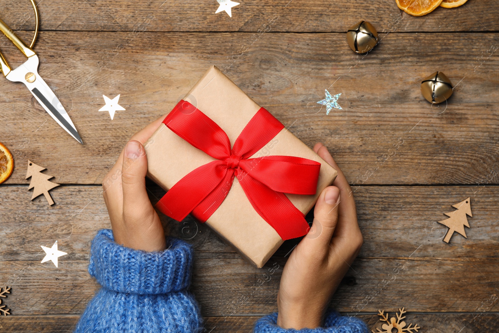 Photo of Young woman holding Christmas gift on wooden background, flat lay