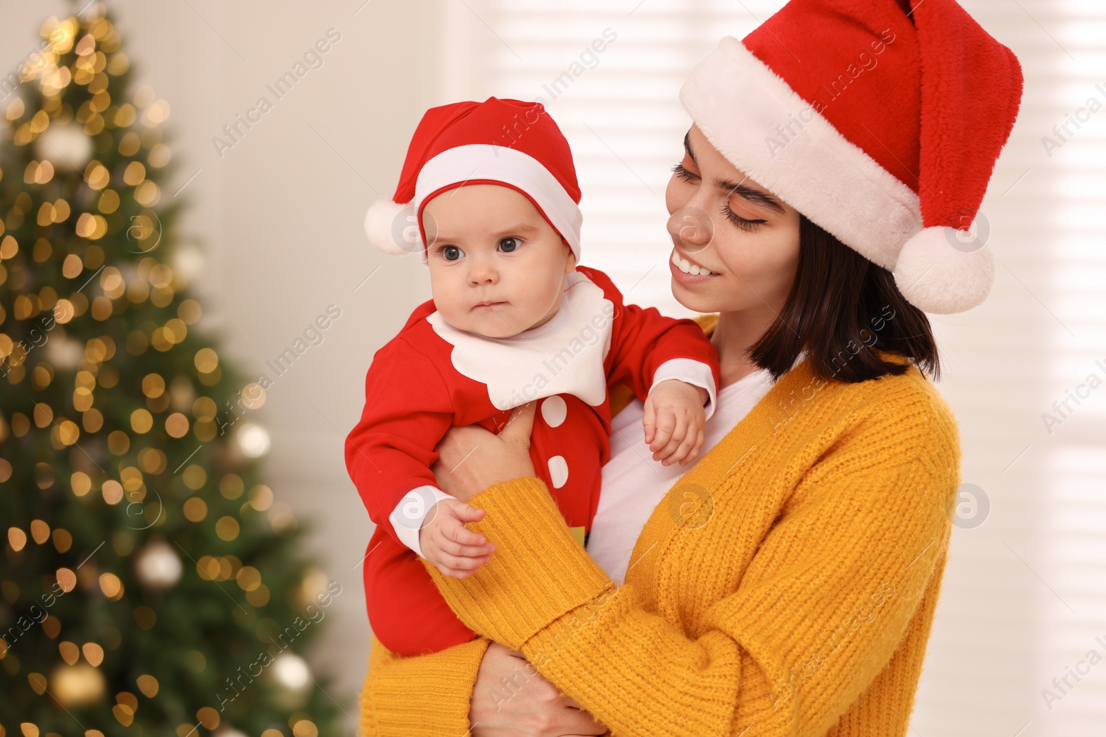 Photo of Happy young mother with her cute baby against blurred festive lights. Winter holiday