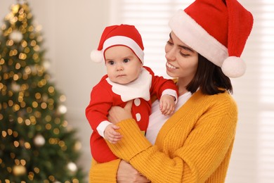 Happy young mother with her cute baby against blurred festive lights. Winter holiday