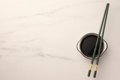 Photo of Bowl with soy sauce and chopsticks on white marble table, top view. Space for text