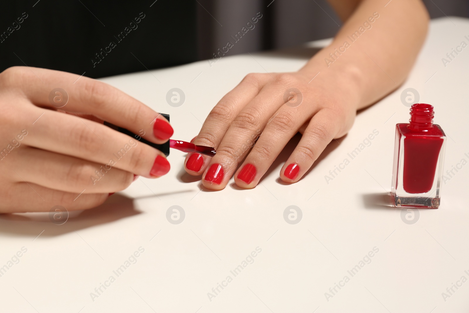 Photo of Woman applying nail polish at table, closeup