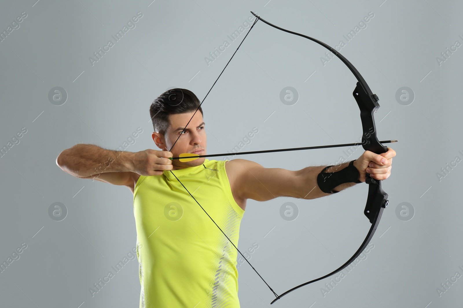 Photo of Man with bow and arrow practicing archery on light grey background