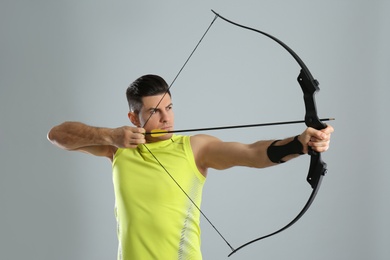 Man with bow and arrow practicing archery on light grey background