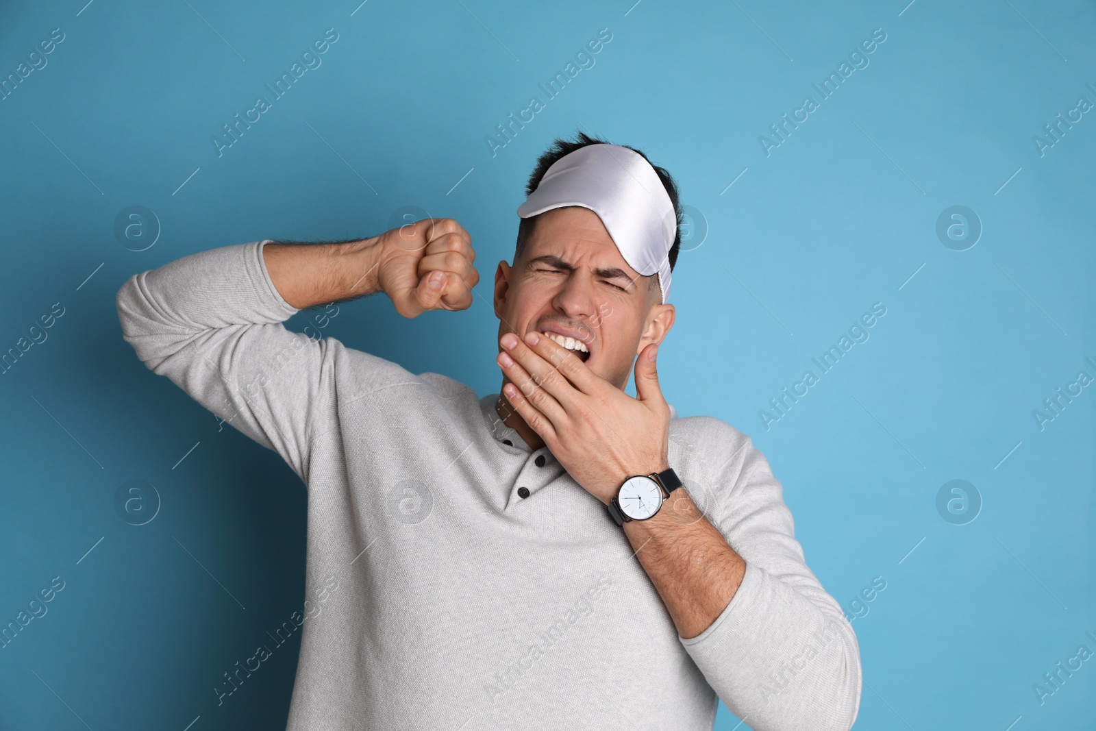 Photo of Tired man with sleeping mask yawning on light blue background