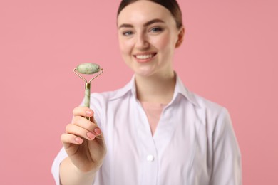 Photo of Cosmetologist with facial roller on pink background, selective focus