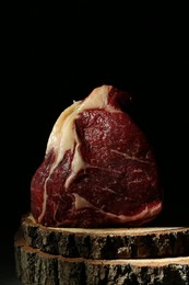 Piece of raw beef meat on decorative wooden stand against black background, closeup