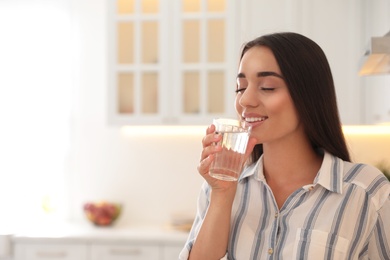 Photo of Young woman drinking pure water from glass in kitchen. Space for text