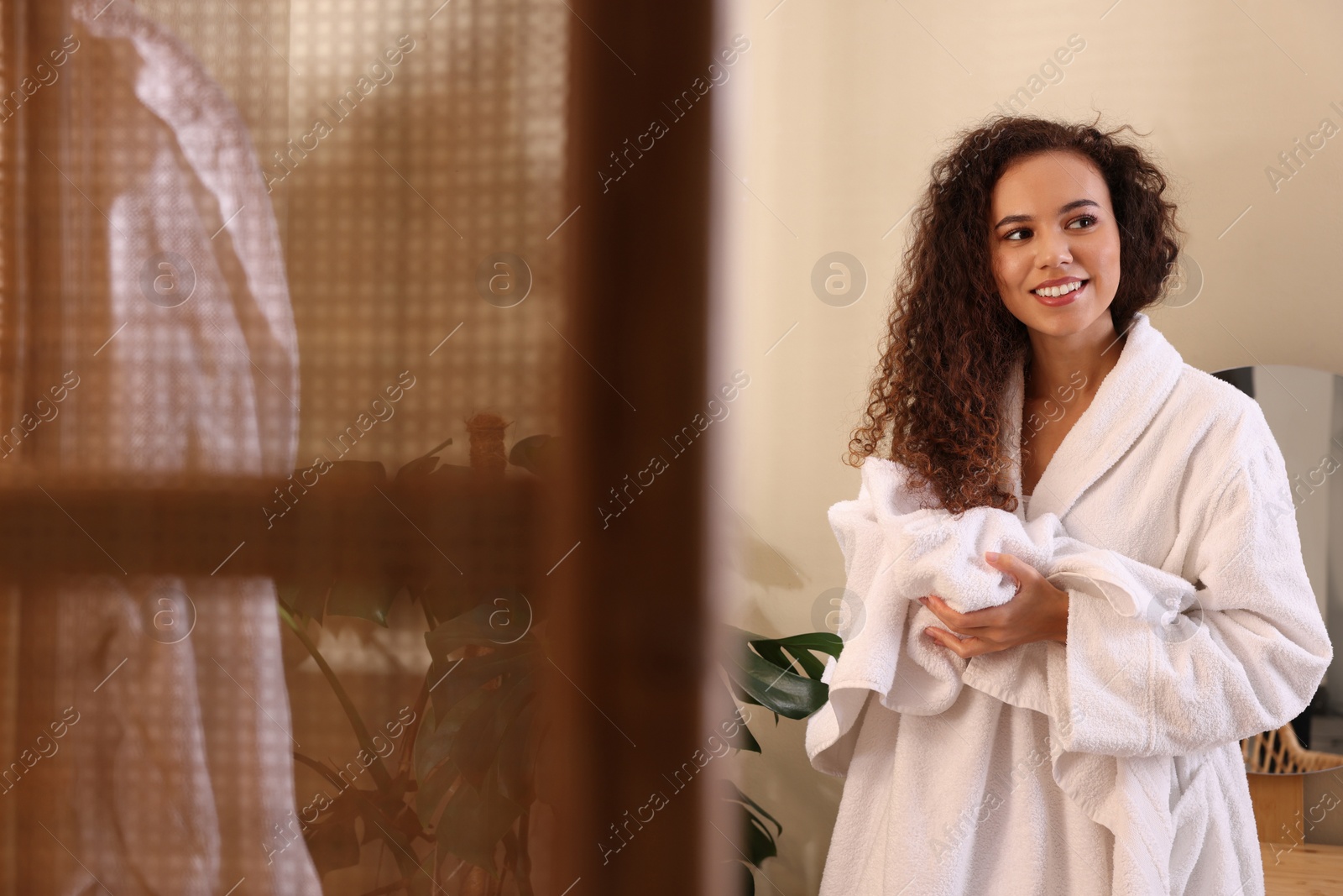 Photo of Beautiful African American woman in bathrobe drying hair with towel at home, space for text