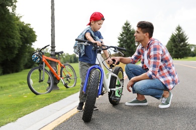 Photo of Dad teaching son to ride bicycle outdoors