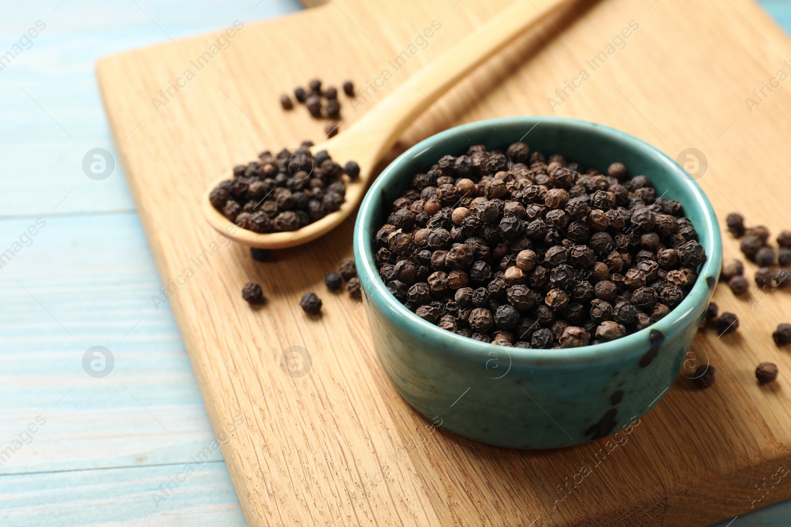 Photo of Aromatic spice. Black pepper in bowl on light blue wooden table, closeup