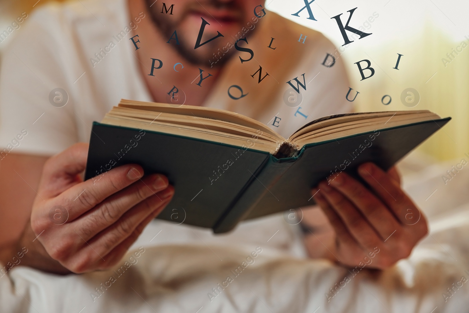 Image of Young man reading book with letters flying over it on bed at home, closeup