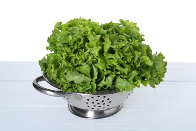 Photo of Metal colander with fresh lettuce on table against white background