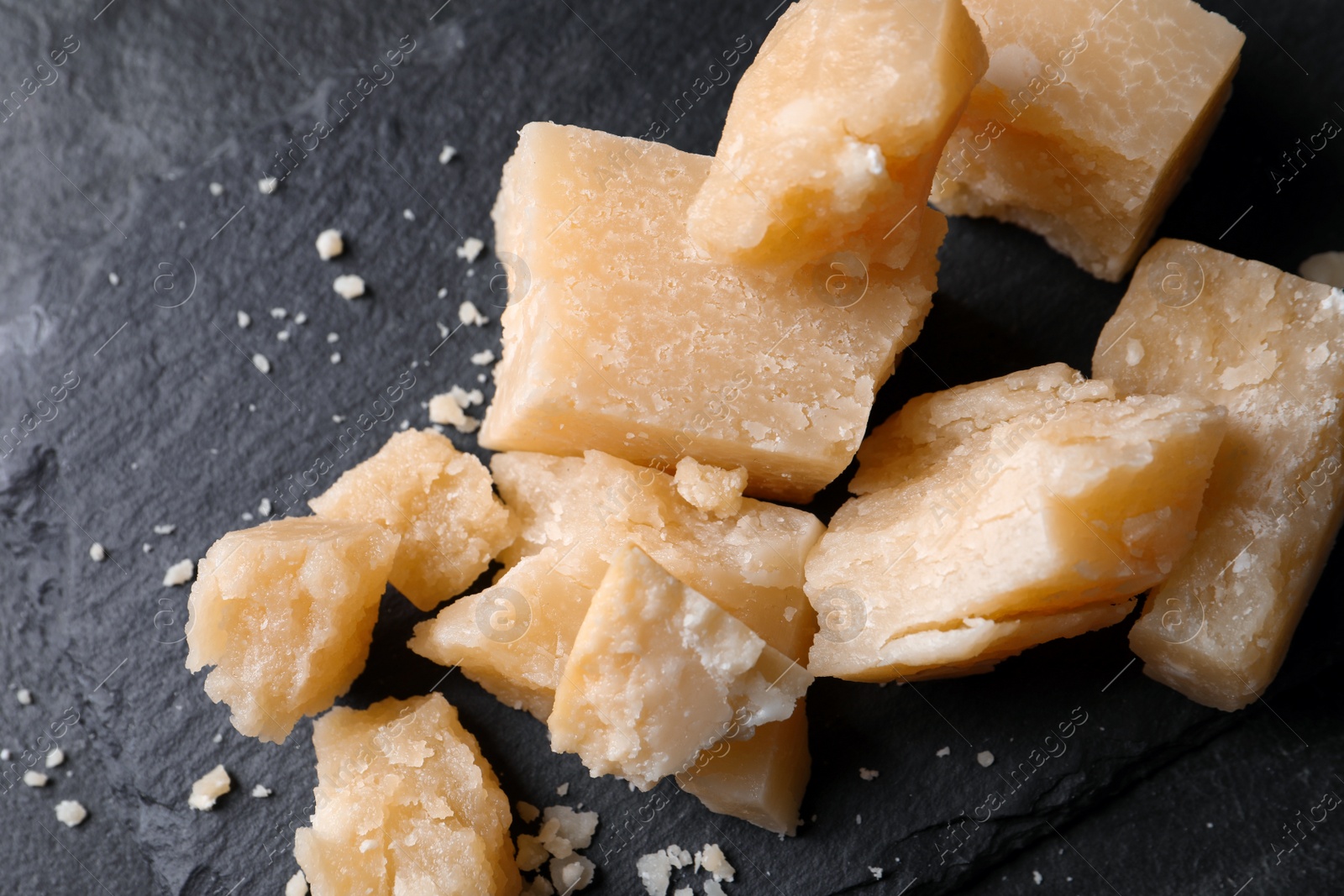 Photo of Pieces of delicious parmesan cheese on slate plate, top view