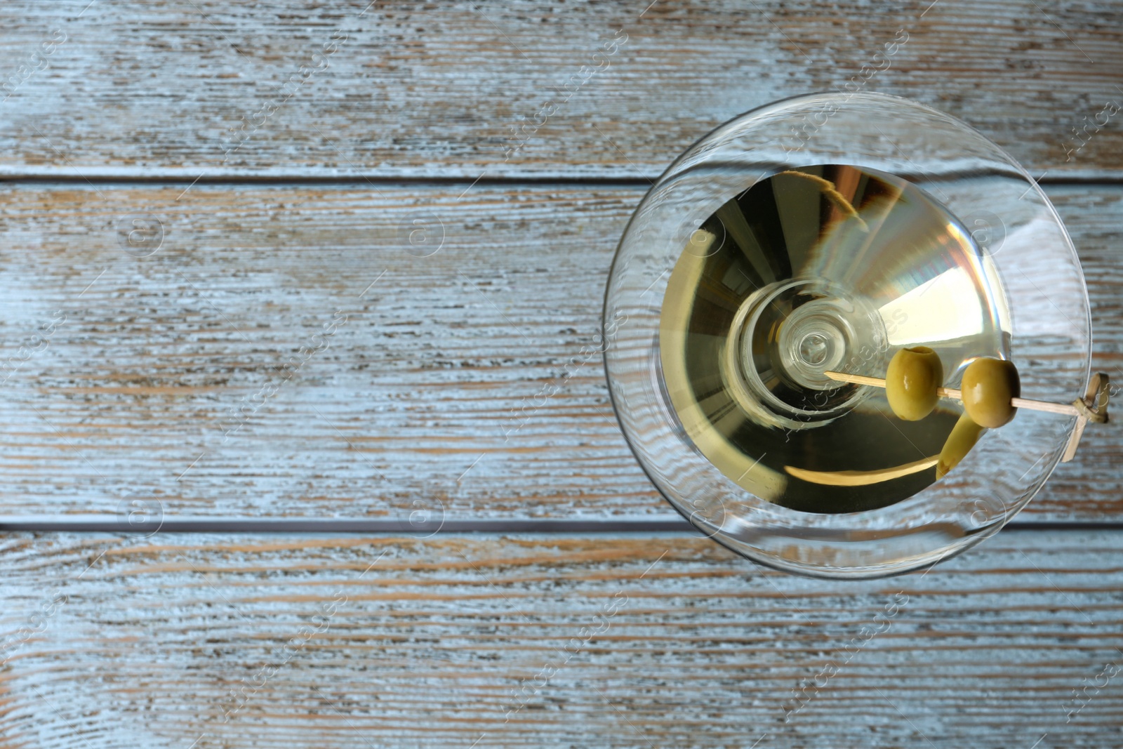 Photo of Glass of Classic Dry Martini with olives on wooden table, top view. Space for text